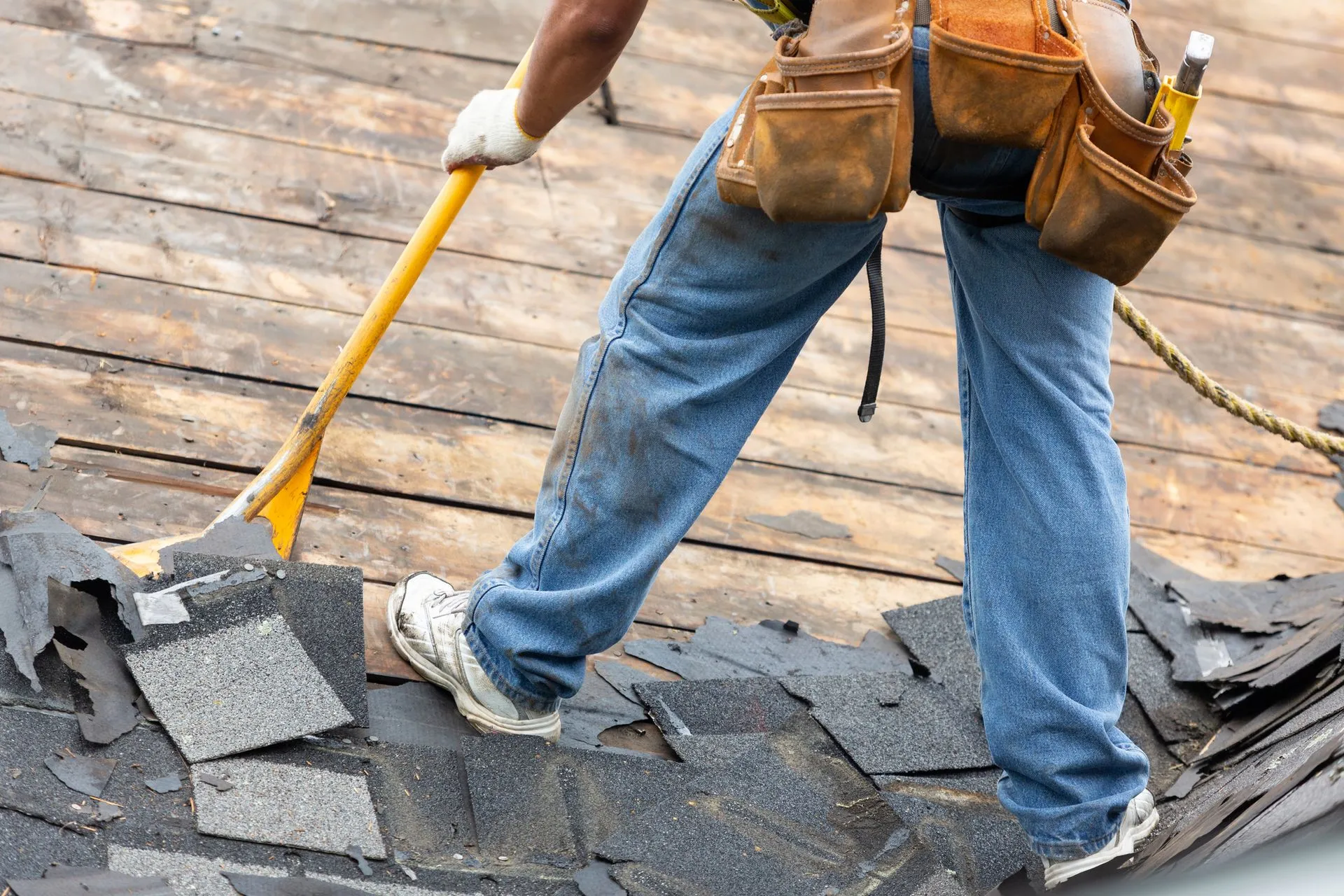 A roofer removing old shingles from the roof of a house.