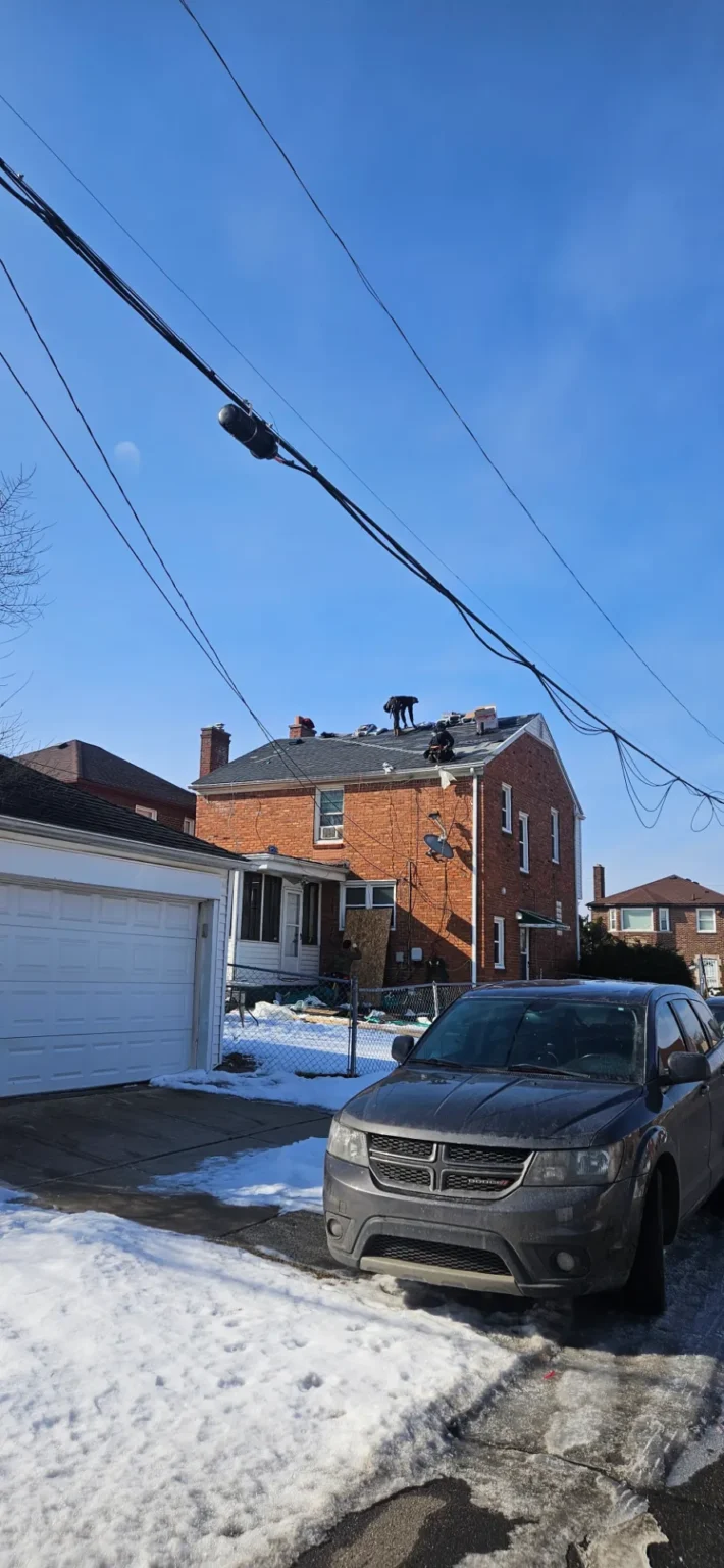 T&M Roofing crew working on a brick home with a garage roof in Metro Detroit