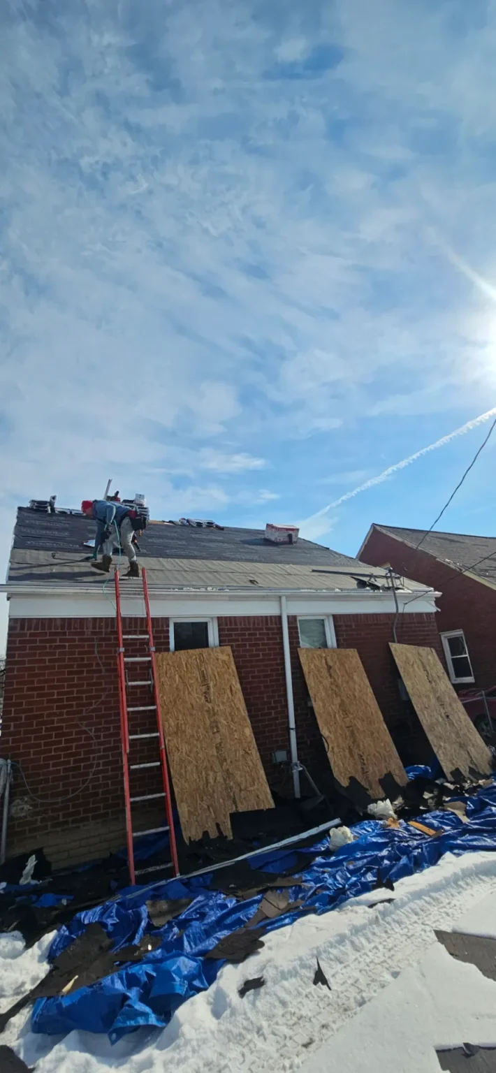 T&M Roofing crew on a ladder carrying plywood decking for a roof replacement